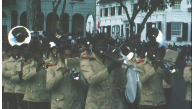 Foto van het gloednieuwe Surinaamse militaire muziekkorps dat door de straten van Paramaribo paradeert
